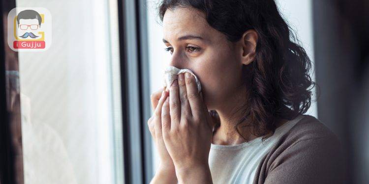 Shot of sad young woman crying while looking through the window at home.